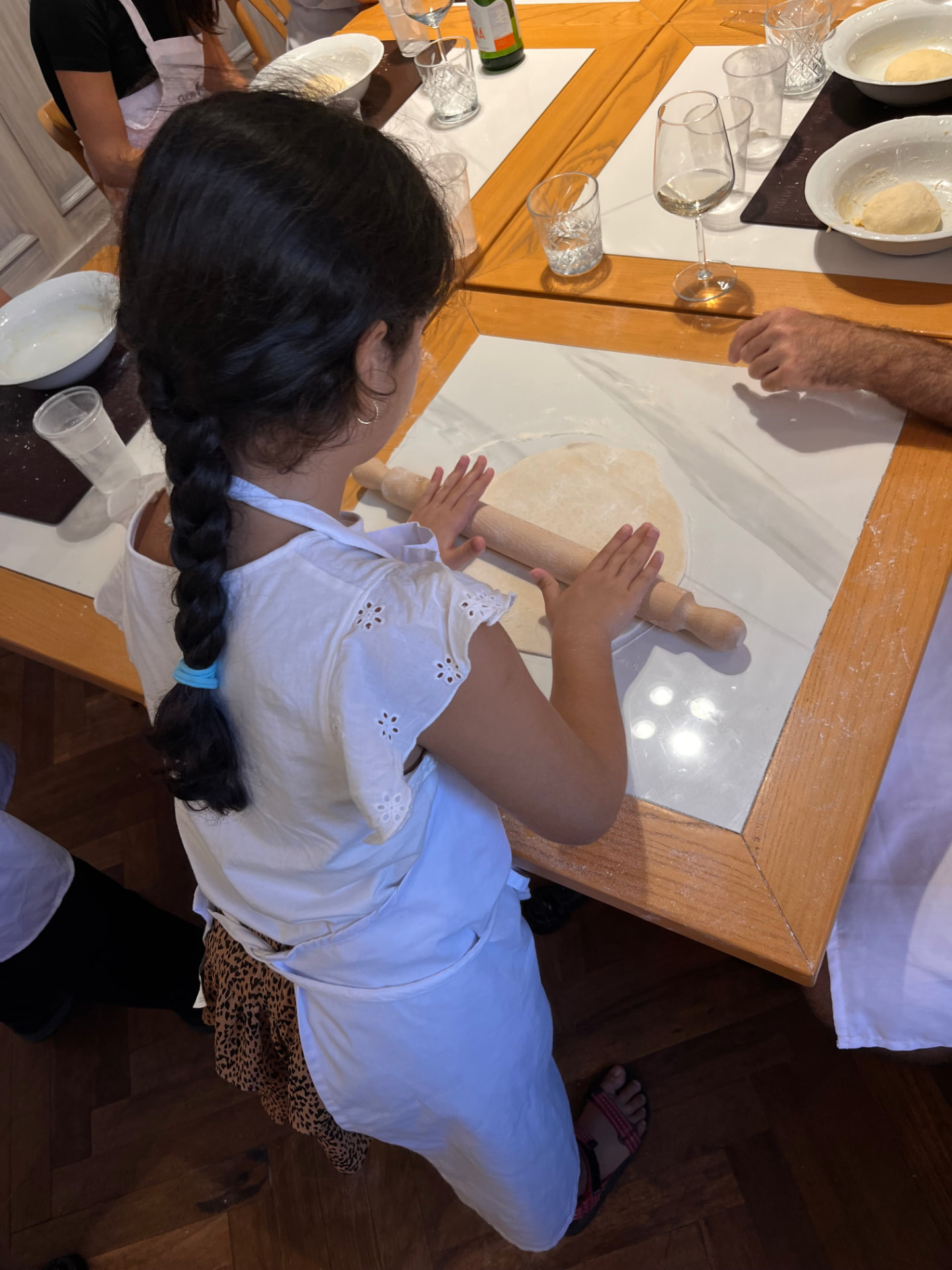 Bambina stende l'impasto della pizza col mattarello durante la pizza class per famiglie a Roma