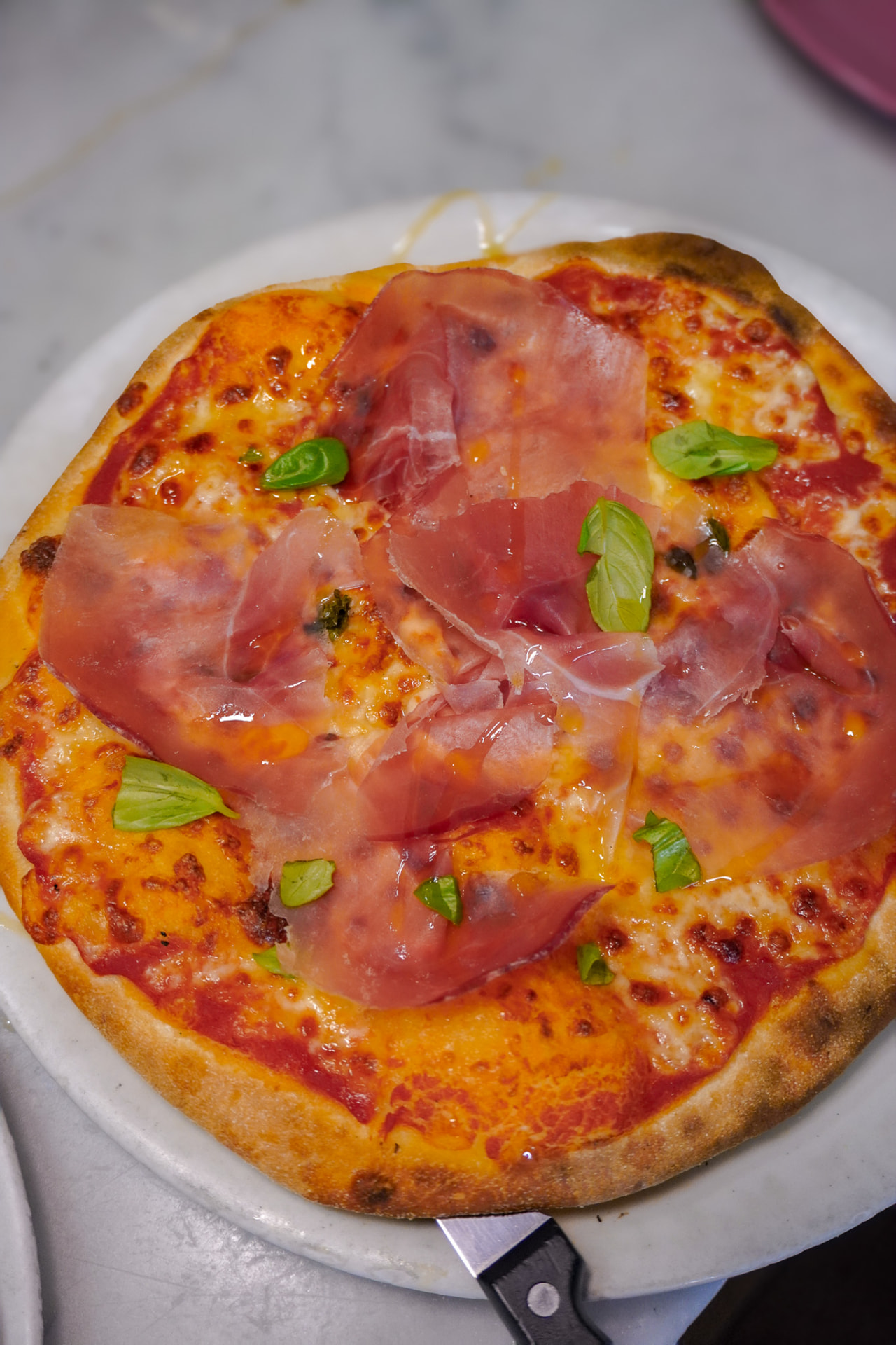 Pizza fatta a mano con prosciutto crudo, mozzarella e basilico fresco cotta nel forno durante la pizza class a Roma